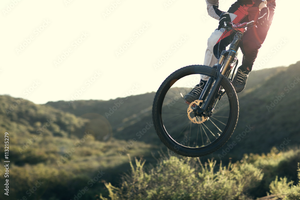 Young man jumping on mountain bike in green valley Young man jumping on mountain bike in green valley