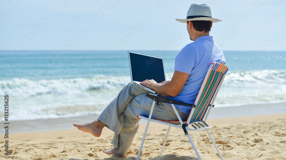 Business man using computer, tropical beach outdoors. Back view