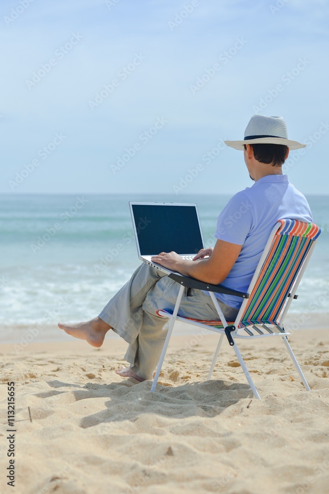 Back side view of relaxed man using laptop, beach background, outside summertime