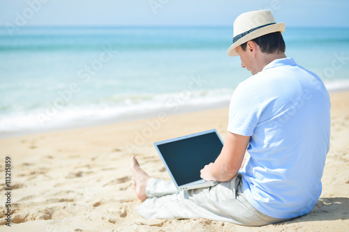 Handsome relaxed man using laptop, beach background back side view