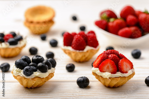 Tartlets with cream  blueberries  raspberries and strawberries on white wooden table. Selective focus.