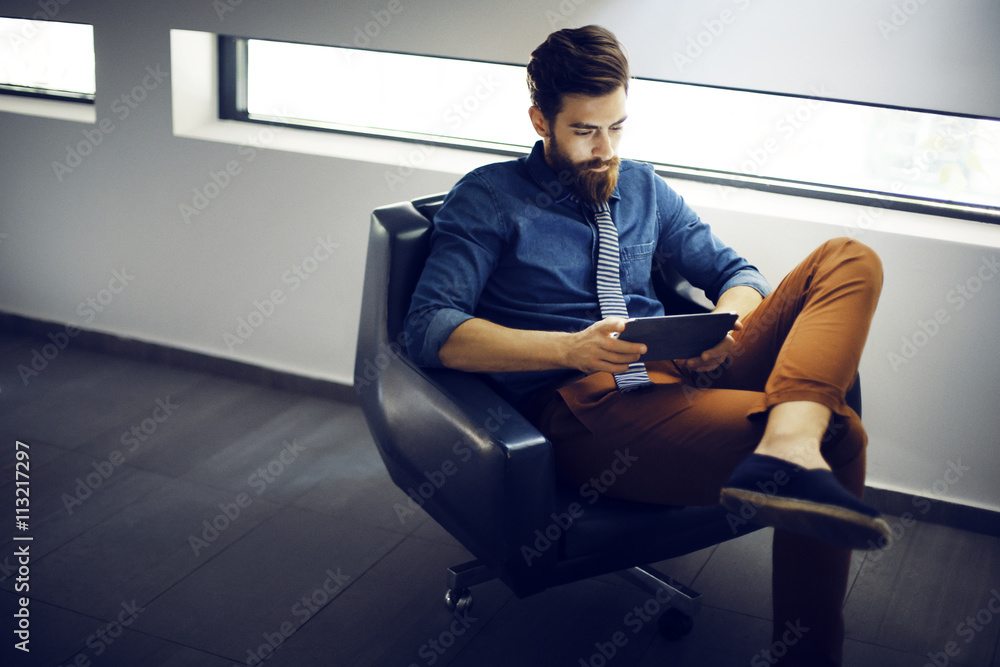 Young man with bear sitting in office and using digital tablet Young man with bear sitting in office and using digital tablet