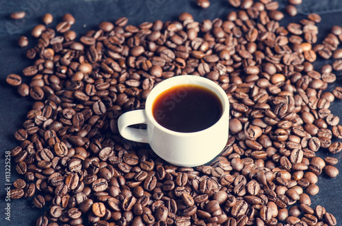 Coffee beans on a black background. Raw coffee beans. Grained product. Hot drink. Close up. Harvesting. Natural background. Energy. In the middle of picture is coffee cup