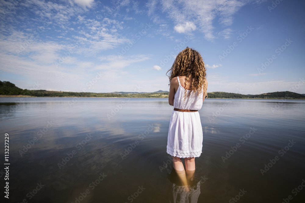 Rear view of female with curly hair, wearing white dress, standing in lake Rear view of female with curly hair, wearing white dress, standing in lake