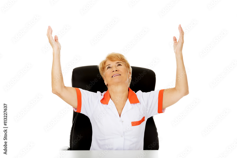 Happy elderly woman sitting behind the desk with hands up Happy elderly woman sitting behind the desk with hands up