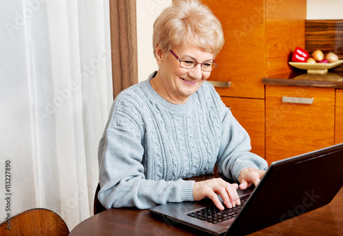 Smile senior sitting at table and using laptop photo