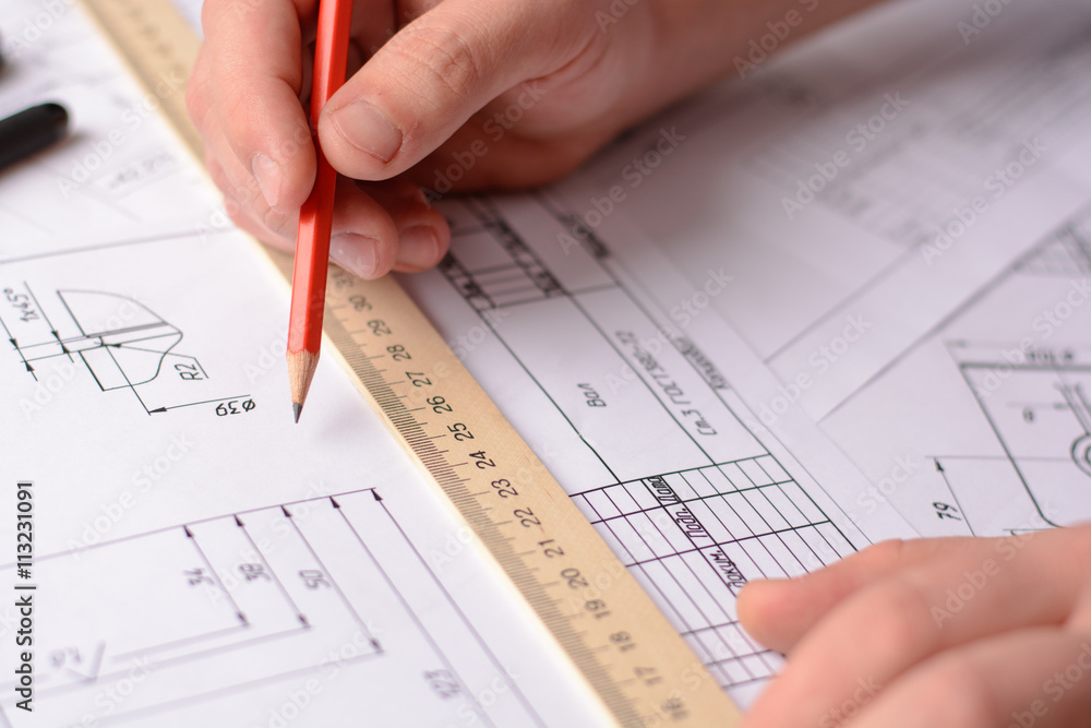 Girl architect draws a plan, graph, design, geometric shapes by pencil on large sheet of paper at office desk. Soft focus Girl architect draws a plan, graph, design, geometric shapes by pencil on large sheet of paper at office desk. Soft focus