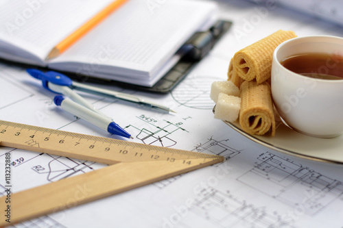 Coffee break. Cup with tea and candies on the table with the figures,drawings and business accessories (ruler, pens, notebooks, compasses)