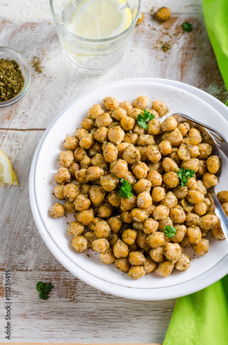 Roasted spicy chickpeas with zaatar or zatar on white bowl on wooden background. Top view