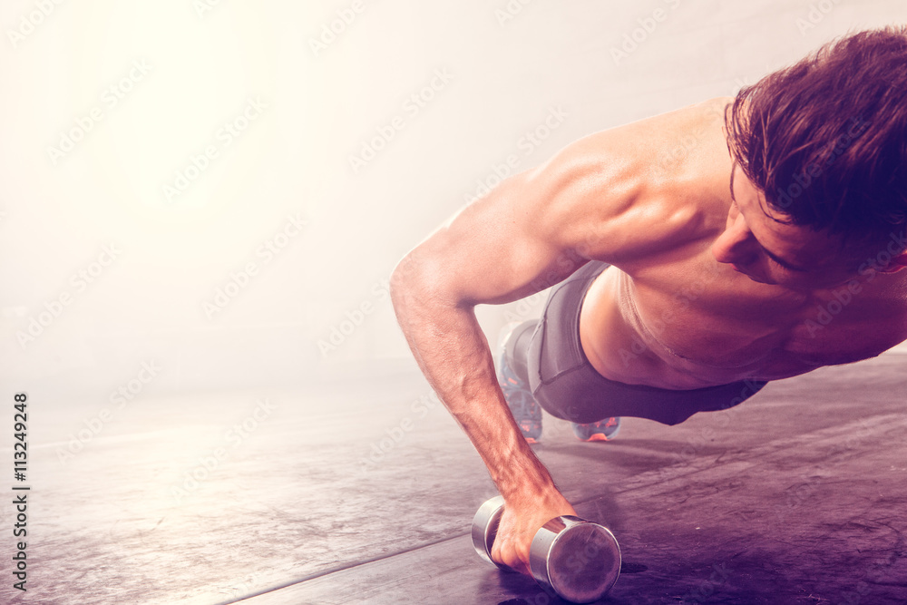Man doing push-up exercise with dumbbell. Strong male doing crossfit workout.
