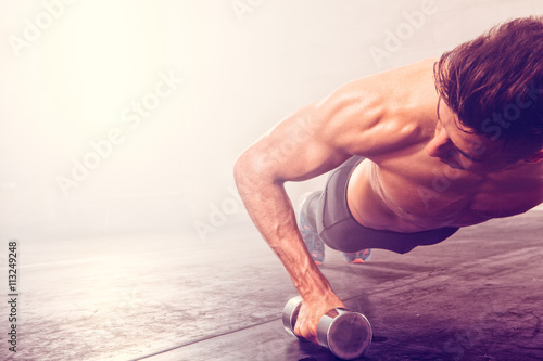 Man doing push-up exercise with dumbbell. Strong male doing crossfit workout.