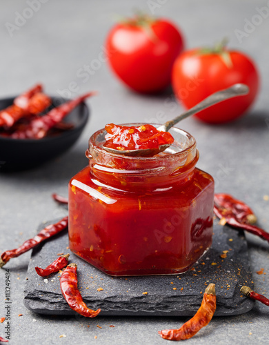 Tomato and chili sauce, jam, confiture in a glass jar on a grey stone background