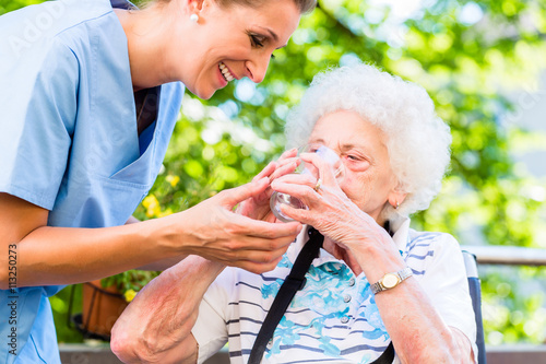 Altenpflegerin gibt Seniorin Glas Wasser zu trinken photo