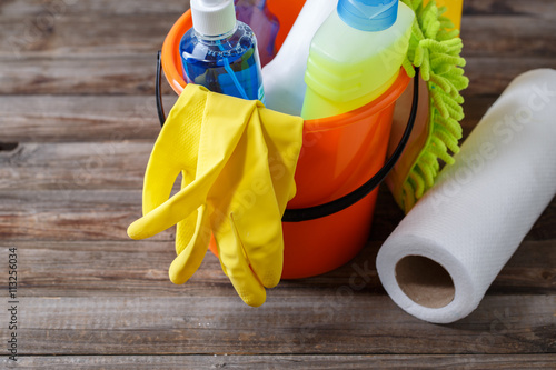 Plastic bucket with cleaning supplies on wood background photo