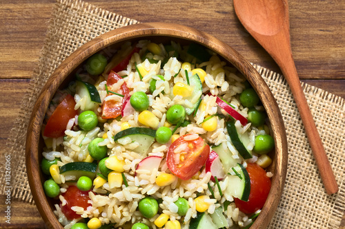 Brown rice salad with cherry tomato, corn, cucumber, radish, pea and chives served in bowl, photographed overhead on dark wood with natural light (Selective Focus, Focus on the top of the salad)