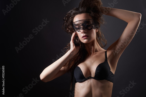 Sensual woman posing over dark background with lace mask on closed eyes