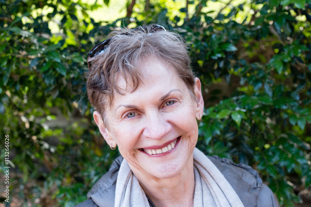 Portrait of older woman smiling with sunglasses on head against green leafy background Portrait of older woman smiling with sunglasses on head against green leafy background