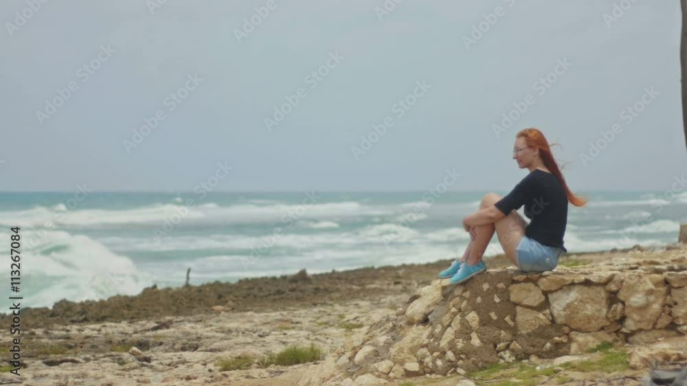 Seductive girl with long red hair sitting on the beach near the storm sea Seductive girl with long red hair sitting on the beach near the storm sea