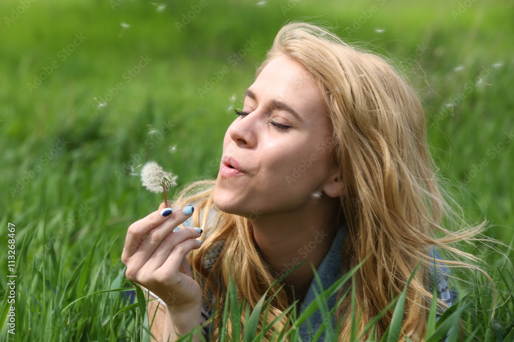 Young beautiful woman with blowball on green grass