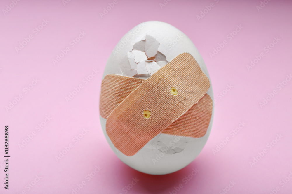 Cracked egg with plaster on pink background Cracked egg with plaster on pink background