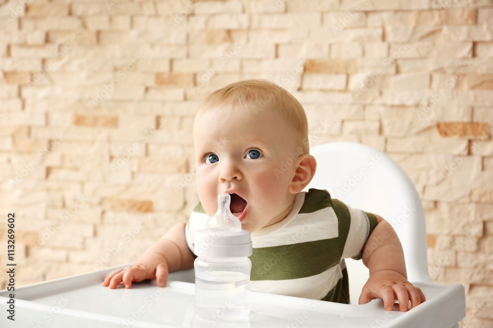 Baby drinking water in a chair on brick wall background Baby drinking water in a chair on brick wall background