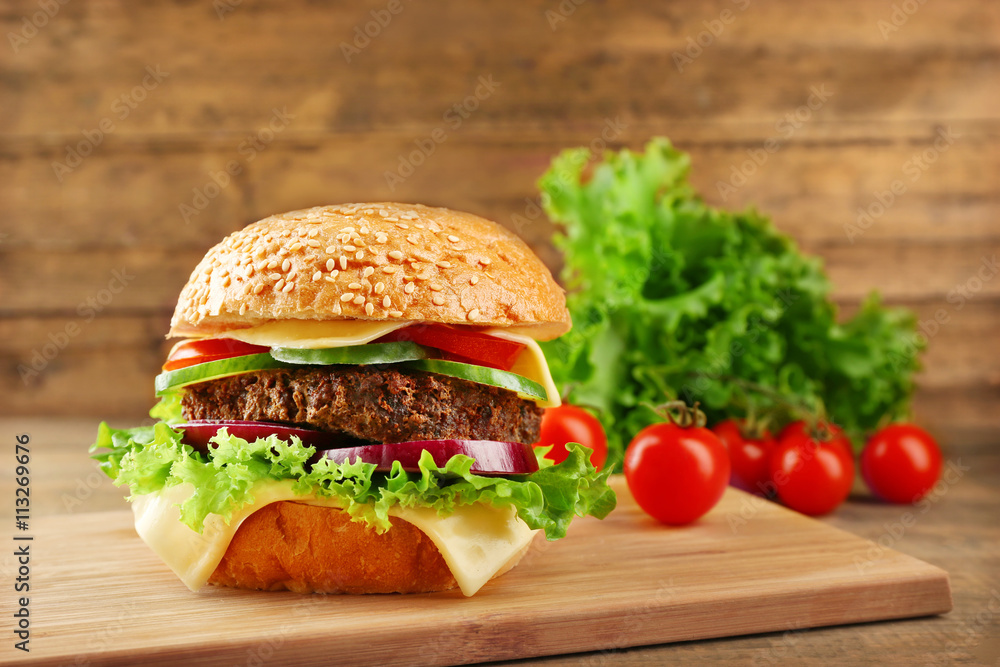 Big hamburger with vegetables on wooden background