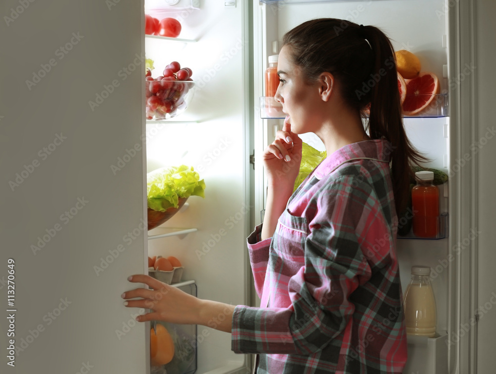 Young beautiful woman looking into fridge at night Young beautiful woman looking into fridge at night
