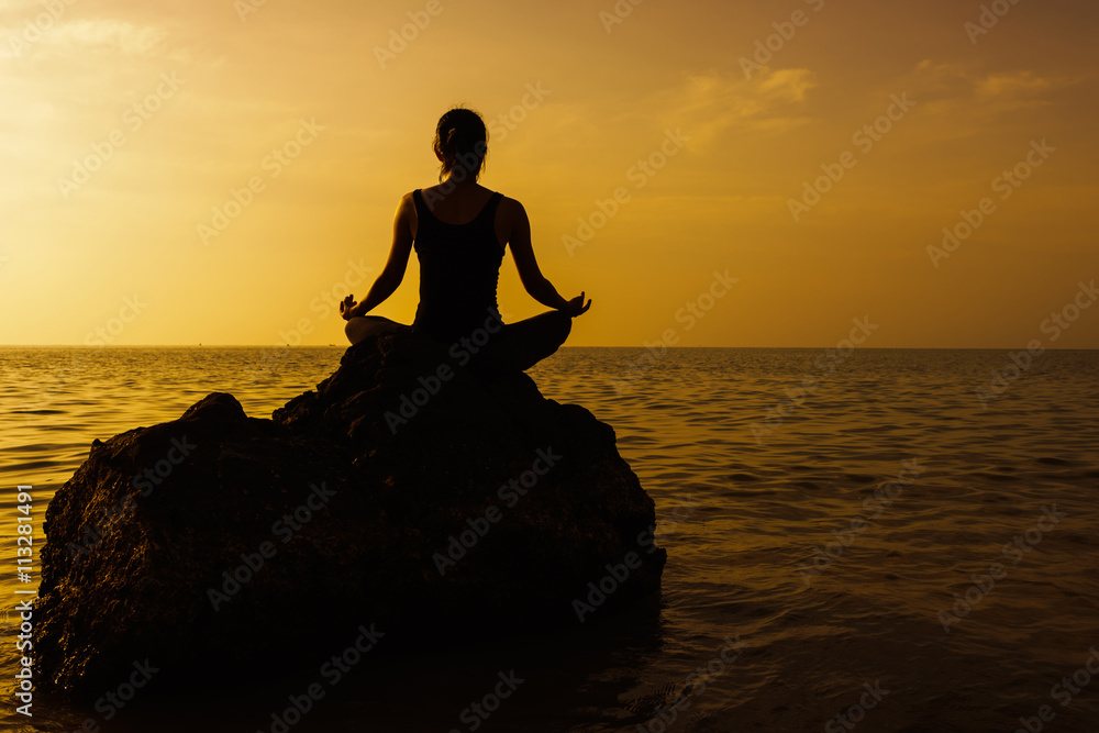 Silhouette of woman practicing yoga on the rock during a beautif