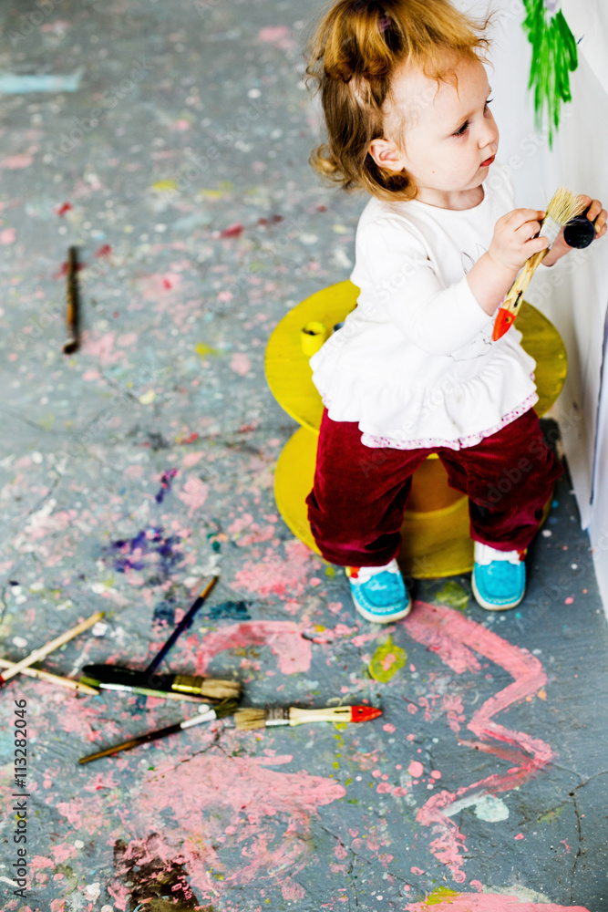 Naklejka premium beautiful little girl draws on the wall with paints, brushes for painting, freehand drawing