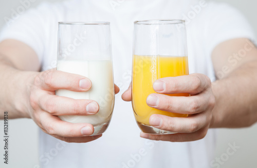 Male hands holding a glass of orange juice and a glass of milk