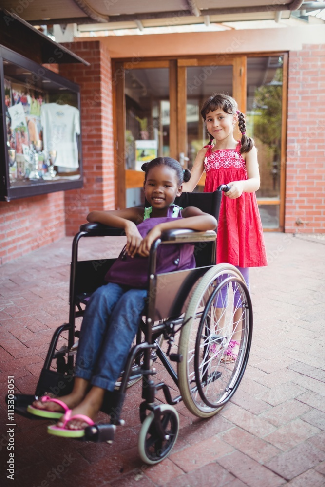 Girl pushing a friend in a wheelchair on a sunny day