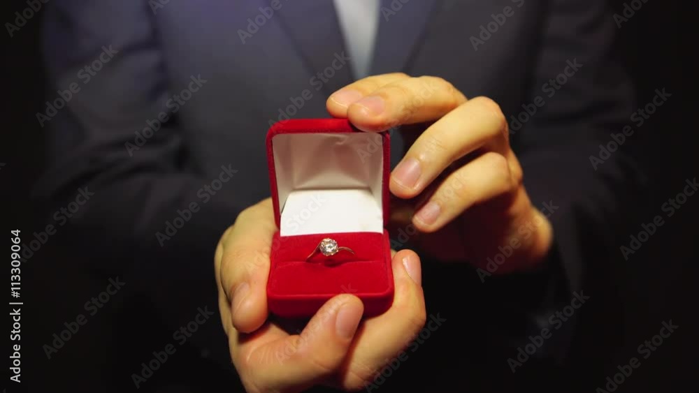 Man in a blue suit gives a ring with a diamond in a red box Man in a blue suit gives a ring with a diamond in a red box