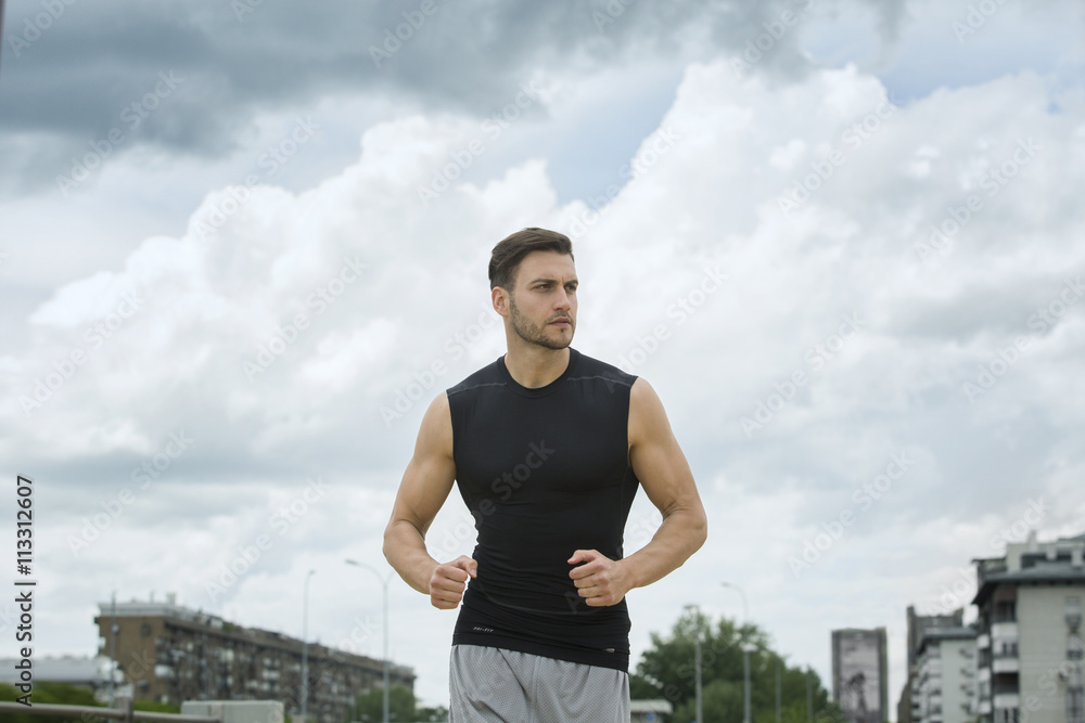 Muscular man jogging outdoors, dramatic sky backdrop