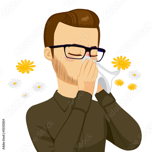 Young brown haired man sneezing blowing nose on white tissue because of spring allergy