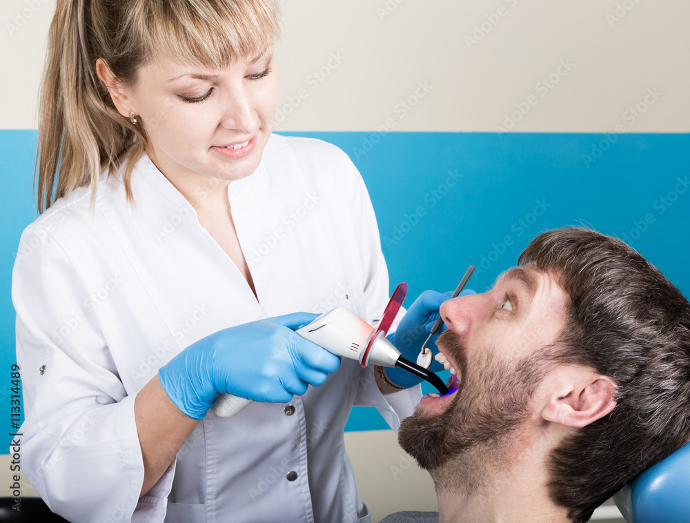 Doctor examines the oral cavity on tooth decay. Caries protection. Tooth decay treatment. Dentist working with dental polymerization lamp in oral cavity