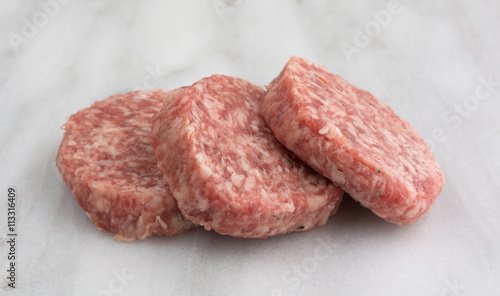 Fresh sausage patties on a marble cutting board side view.