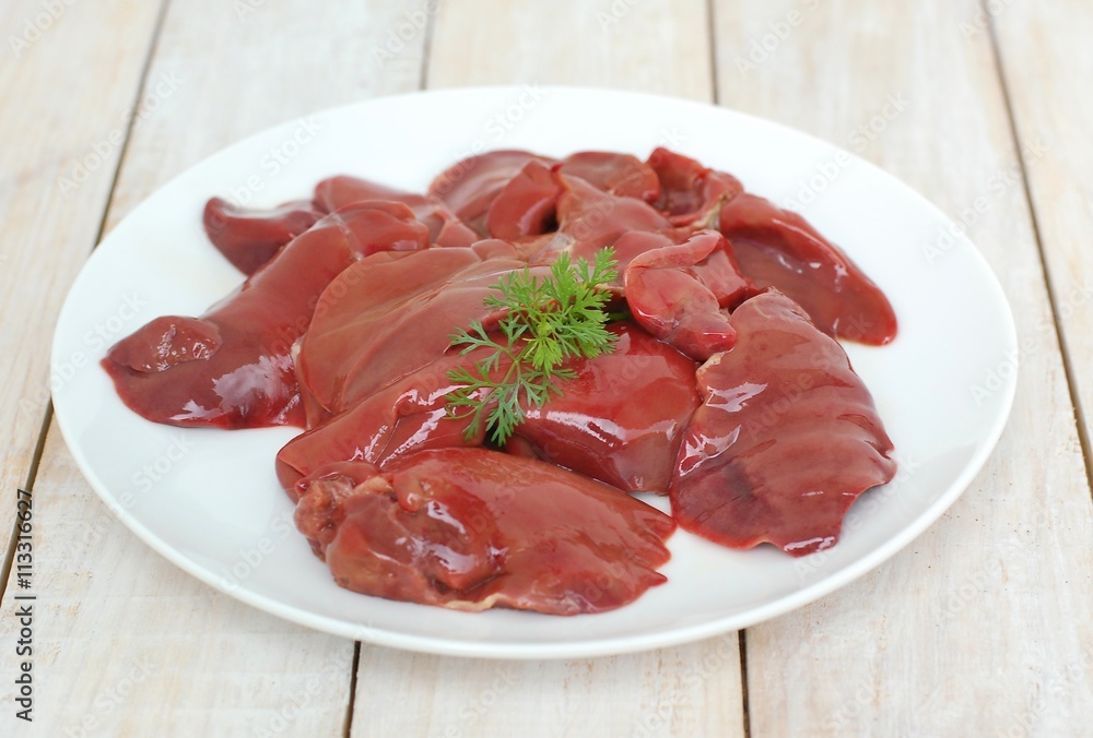 Raw liver on the white plate on the wooden background