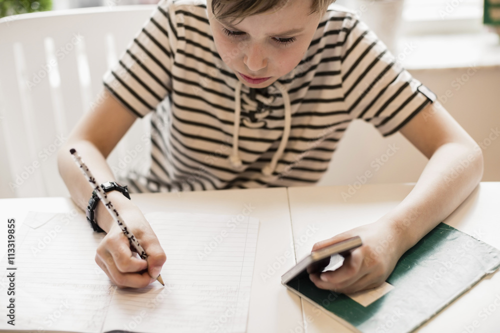 High angle view of boy using mobile phone while studying at table in house High angle view of boy using mobile phone while studying at table in house