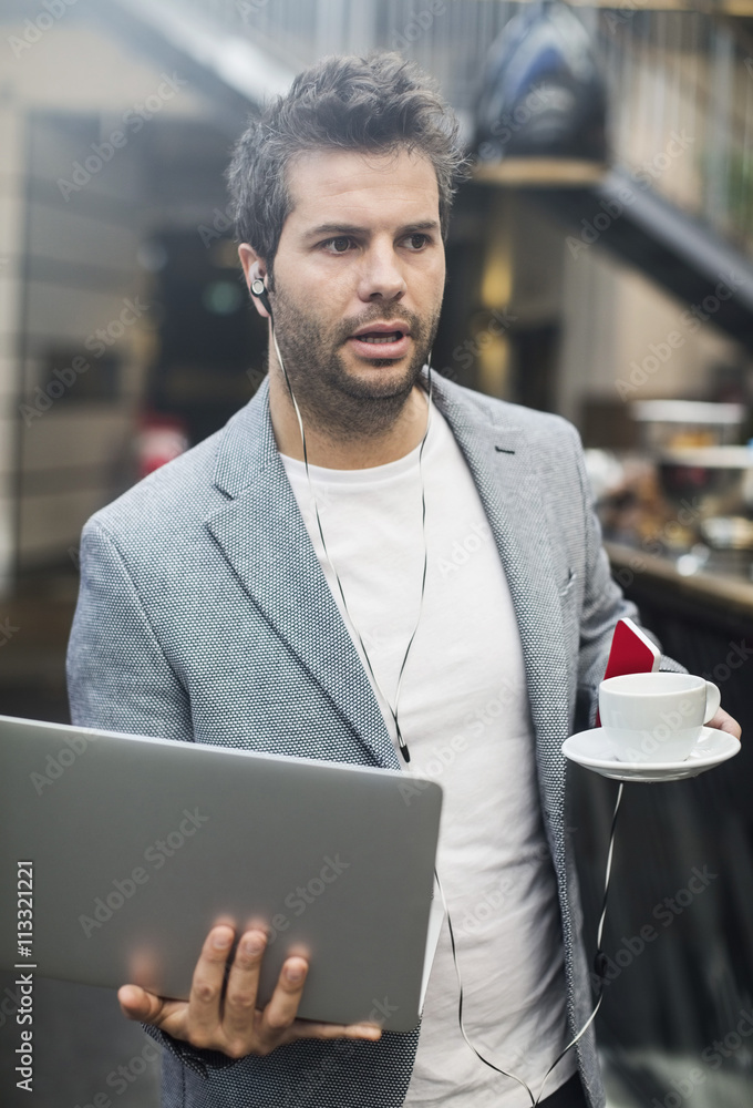 Mid adult man holding laptop and coffee in cafe Mid adult man holding laptop and coffee in cafe