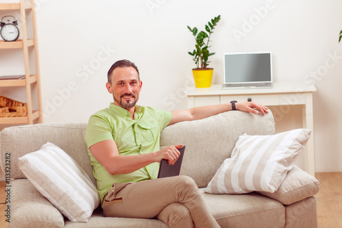 Picture of handsome man using tablet PC for working at home. Happy freelance man working from home sitting on sofa or couch.