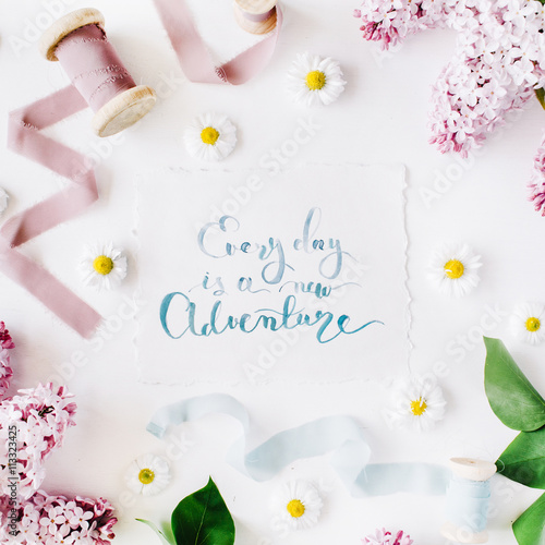 inspirational quote "everyday is a new adventure" written in calligraphy style on paper with wreath frame with lilac and chamomile isolated on white background. flat lay, overhead view, top view © Floral Deco