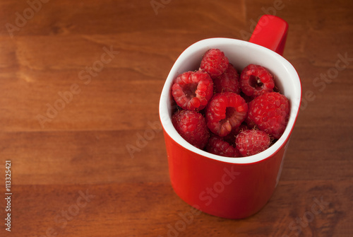 Raspberry in red mug on wood background
