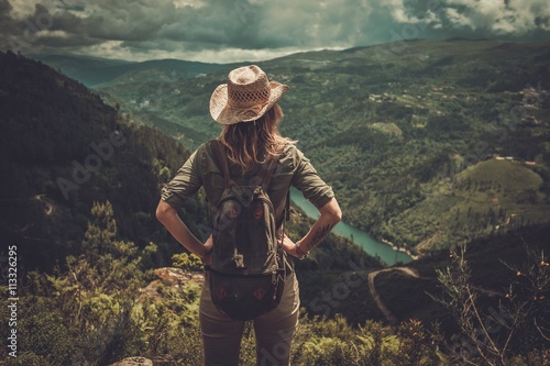 Woman hiker with backpack enjoying amazing valley landscapes on a top of mountain. photo