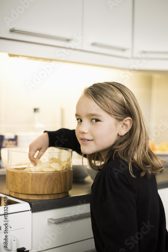 Side view portrait of girl eating potato chips at kitchen counter photo