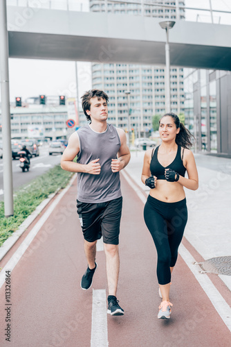 Couple of young handsome caucasian man and woman running into the streets of the city, one overlooking left, the other right - sportive, fitness, healthy concept