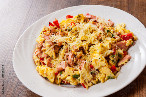 scrambled eggs with ham, vegetables and cheese in a plate on wooden table