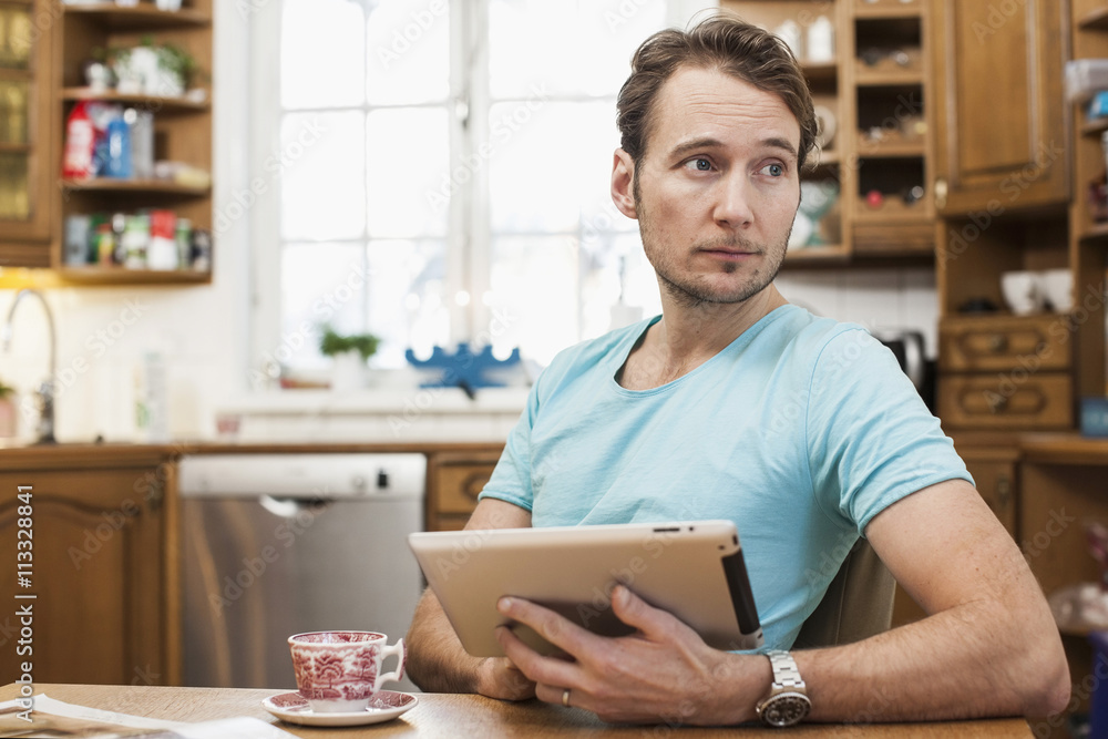 Man holding digital tablet while looking away in kitchen