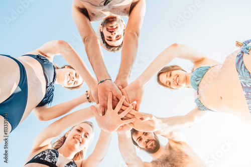 Teamwork. Group of friends in swimsuit on holiday at sea making a pile with their hands in the center of the photo. Bottom view with the sun behind them