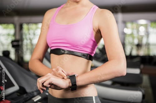 Mid section of woman using smart watch on treadmill