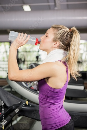 Woman on treadmill drinking water at gym